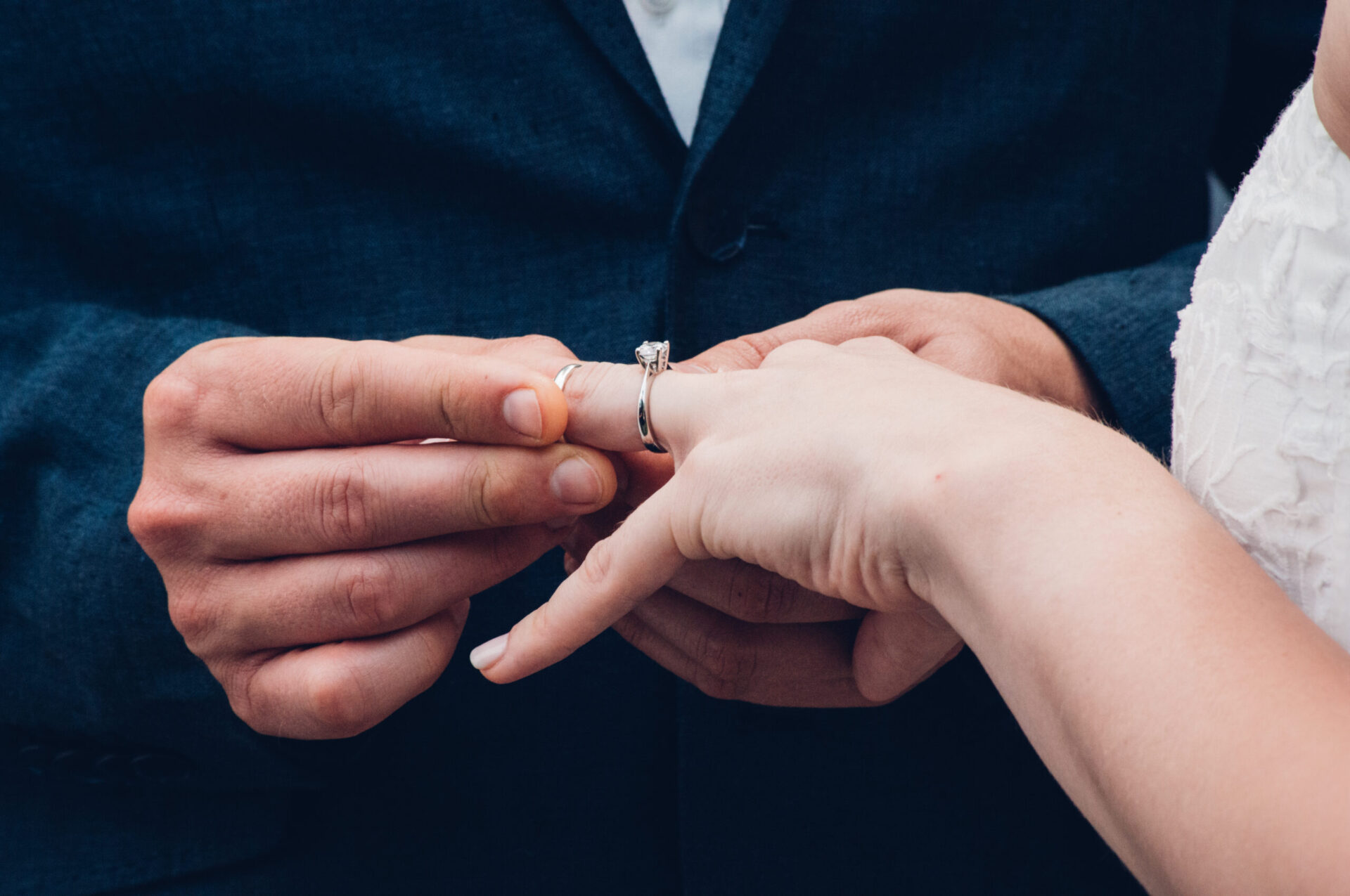Person in suit putting a wedding ring on another person's finger.